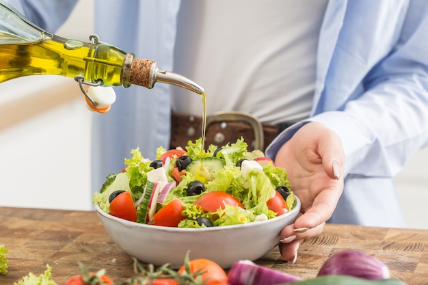 Mujer joven vertiendo aceite de oliva en la ensalada. Concepto de alimentación saludable.