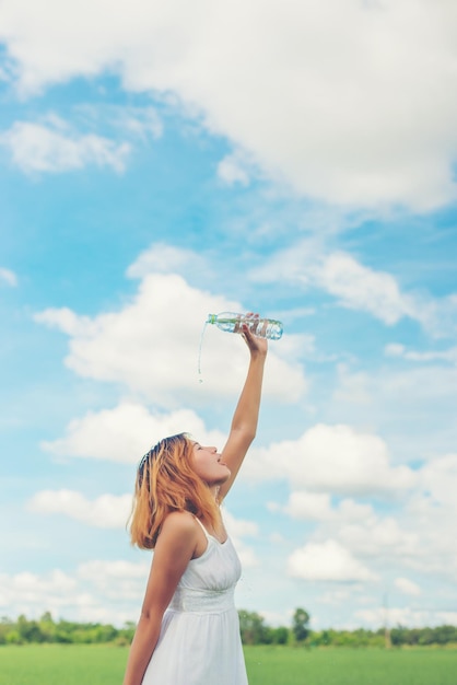 Foto mujer joven vertiendo agua en la cabeza mientras está de pie contra el cielo nublado