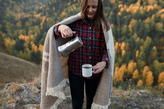 Mujer joven vertiendo café en las montañas