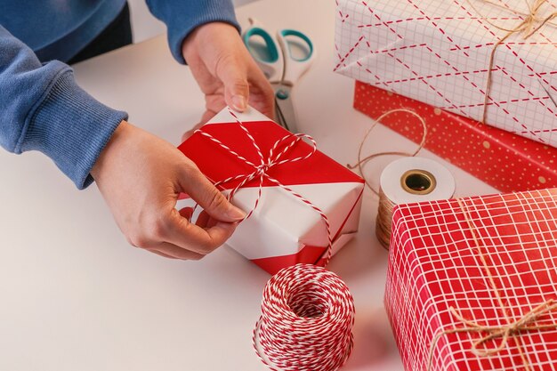 Una mujer joven vestida de azul está envolviendo, empaquetando un regalo de Navidad para niños con un envoltorio hermoso, rojo y blanco con una luz brillante, estilo de vida.