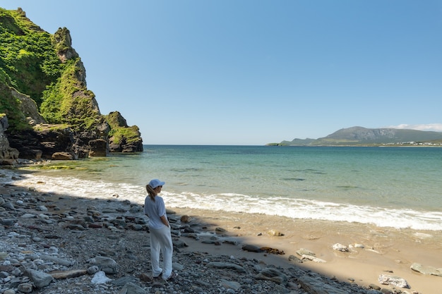 Mujer joven vestida de blanco mirando a la playa rocosa de Keel Beach Achill Island Irlanda