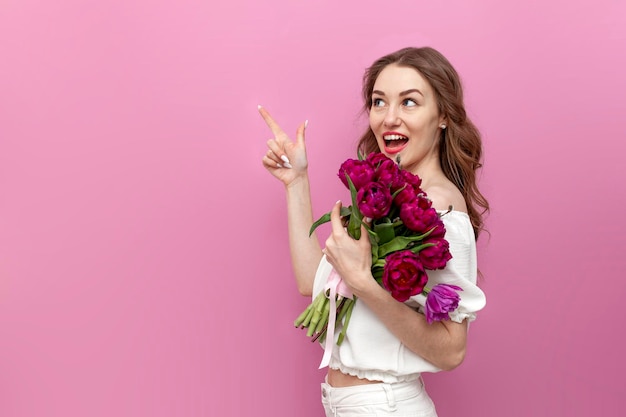 Mujer joven vestida de blanco sosteniendo un ramo de tulipanes rosas y señalando con la mano el espacio de la copia