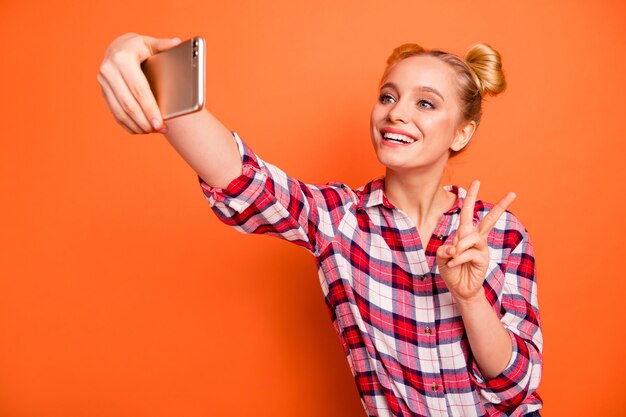 Mujer joven vestida con una camisa de cuadros escoceses aislado en naranja con su teléfono