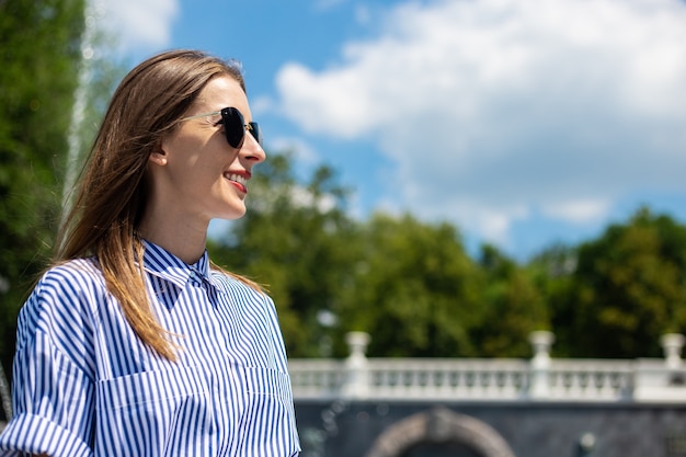 Mujer joven vestida y gafas se sienta cerca de una fuente en el parque.