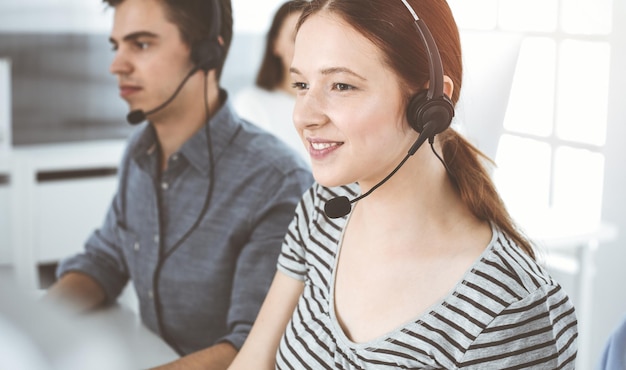 Foto mujer joven vestida de manera informal usando auriculares y computadora mientras habla con los clientes en línea