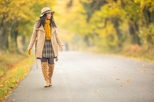 Mujer joven vestida a la moda camina en la colorida naturaleza de otoño.