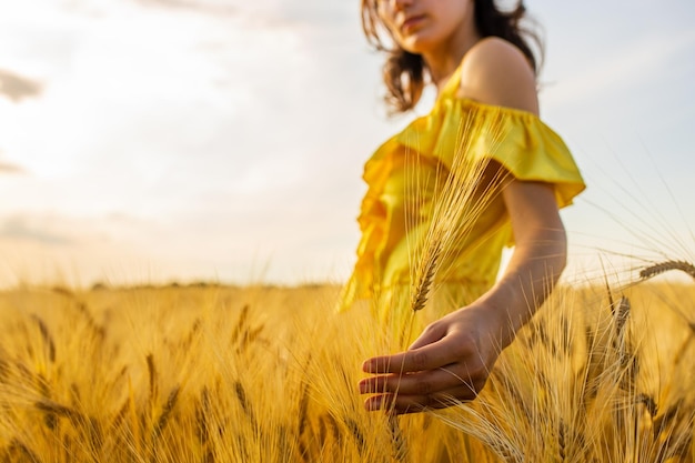 Mujer joven en vestido amarillo de pie en un campo de trigo con amanecer en el fondo