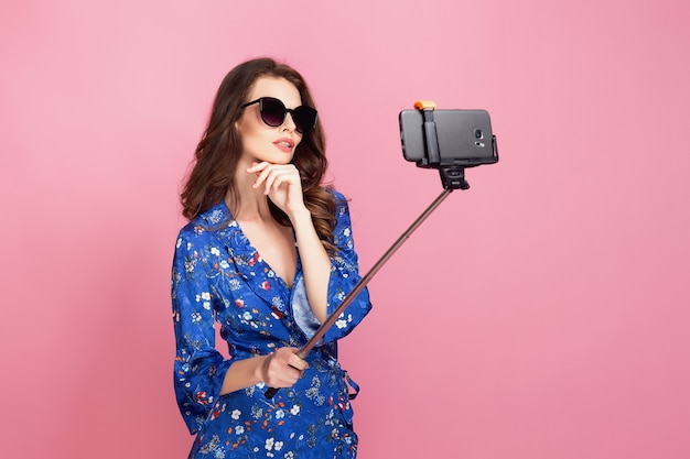 Mujer joven en vestido azul y gafas de sol tomando selfie