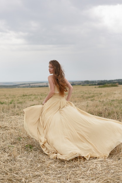 Mujer joven con un vestido beige en campo de trigo