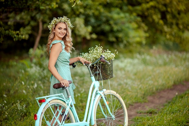 Mujer joven en un vestido con una bicicleta y un ramo de flores silvestres