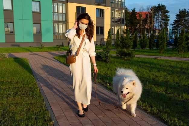 Mujer joven con un vestido blanco paseando a su perro