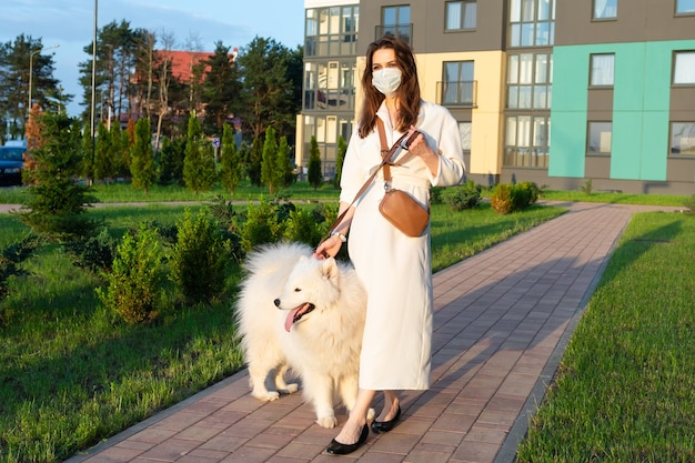 Mujer joven con un vestido blanco paseando a su perro