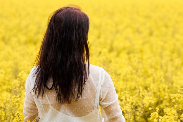 Mujer joven en un vestido blanco de pie en un campo de colza