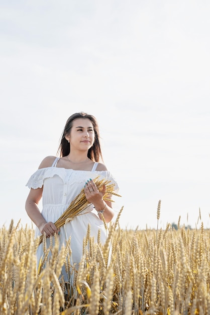 Mujer joven en vestido blanco de pie en un campo de trigo con amanecer en el fondo