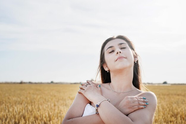 Mujer joven en vestido blanco de pie en un campo de trigo con amanecer en el fondo