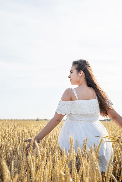 Mujer joven en vestido blanco de pie en un campo de trigo con salida del sol en la vista trasera de fondo