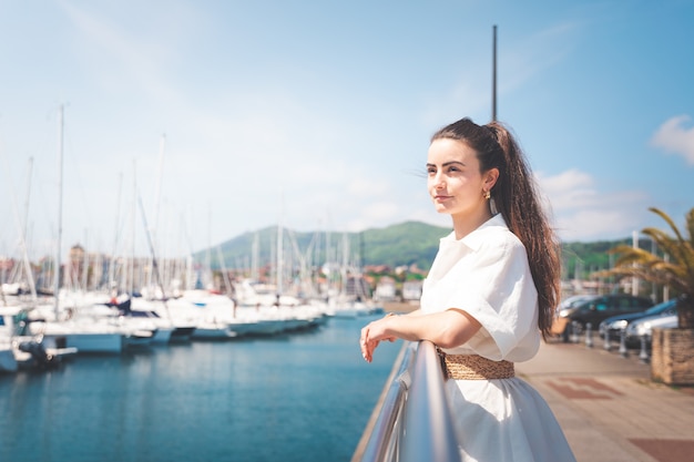 Mujer joven con un vestido blanco en un puerto