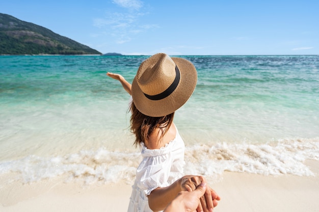 Mujer joven, en, vestido blanco, y, sombrero de paja, tenencia, socio, mano, en la playa