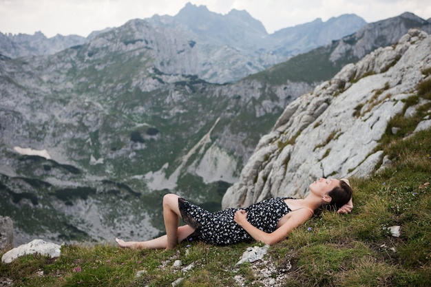 Mujer joven en vestido bonito tendido y descansando en la cima de la montaña