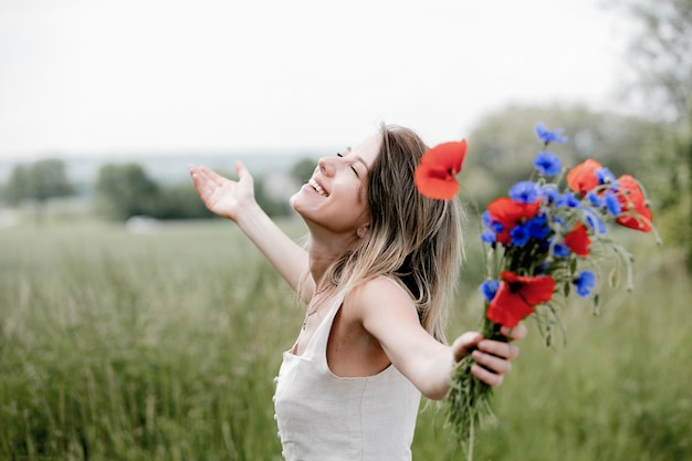 Mujer joven en vestido estancia cerca del campo con ramo de flores Centaurea y amapolas