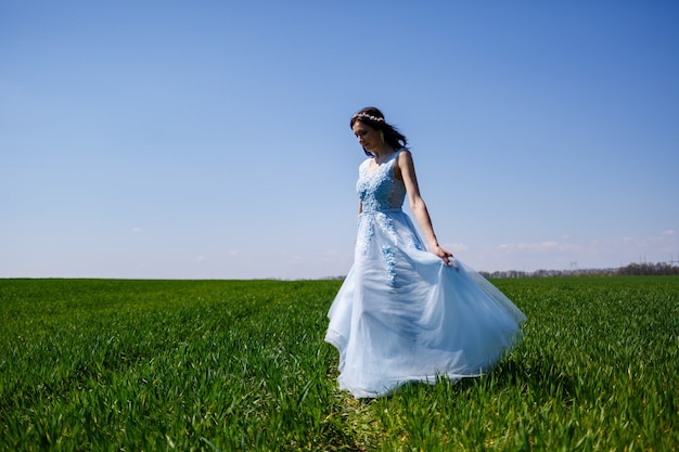 Mujer joven con un vestido largo azul sobre un fondo de campo verde. Retrato de moda de una hermosa niña con una sonrisa en su rostro