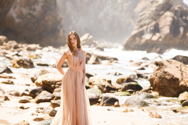 mujer joven en un vestido largo caminando en la playa cerca del océano.