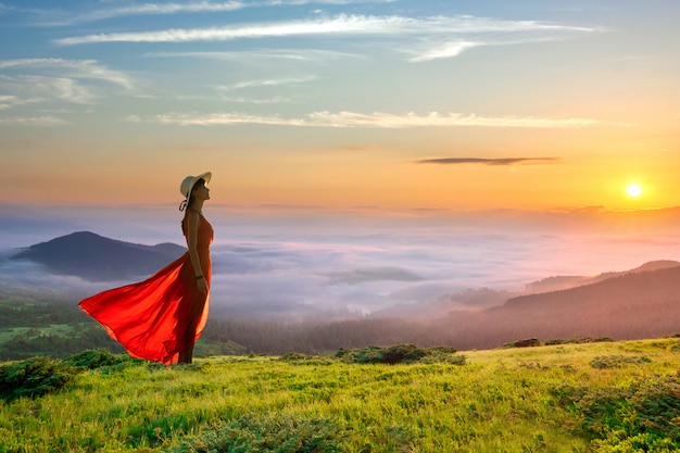 Mujer joven en vestido largo rojo de pie sobre una montaña