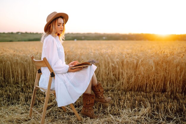 Mujer joven con vestido de lino blanco y sombrero disfrutando de un día soleado en un campo de trigo dorado Belleza de verano