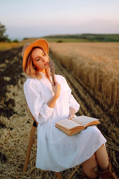 Mujer joven con vestido de lino blanco y sombrero disfrutando de un día soleado en un campo de trigo dorado Belleza de verano