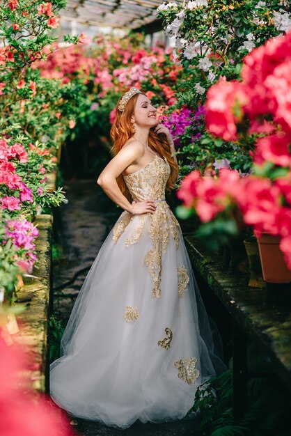 Mujer joven en vestido de lujo de pie en el jardín de flores