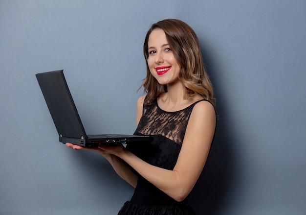 Mujer joven en vestido negro con cuaderno en pared gris