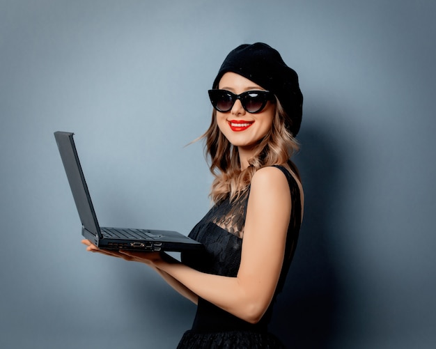 Mujer joven en vestido negro con cuaderno en pared gris