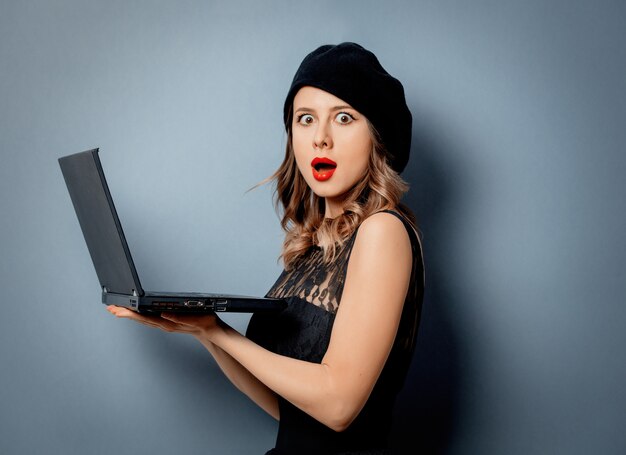 Mujer joven en vestido negro con cuaderno en pared gris