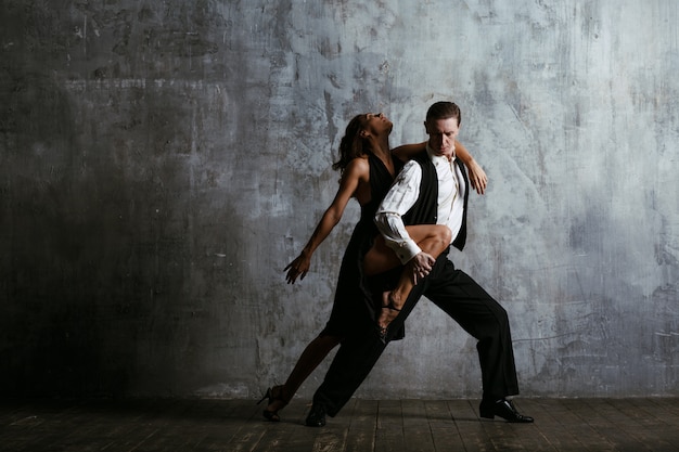 Foto mujer joven en vestido negro y hombre bailar tango