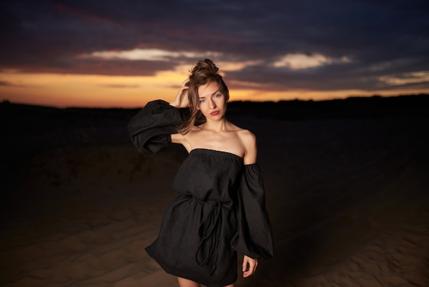 Foto mujer joven, en, un, vestido negro, posar, en, un, playa