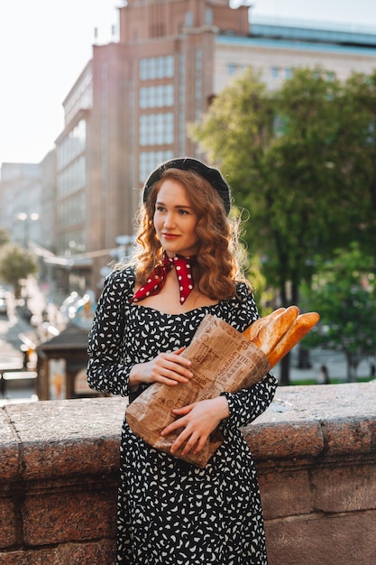 Mujer joven en vestido negro sosteniendo un paquete de papel de baguettes francesas Foto de comida de panadería de pan