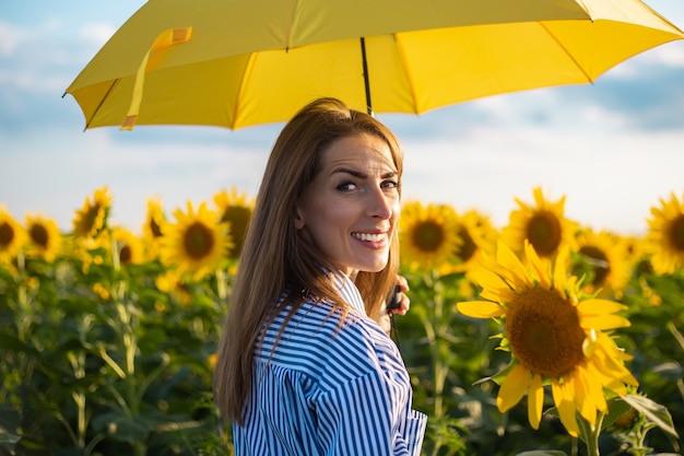 Mujer joven en vestido y paraguas amarillo en un campo de girasoles.