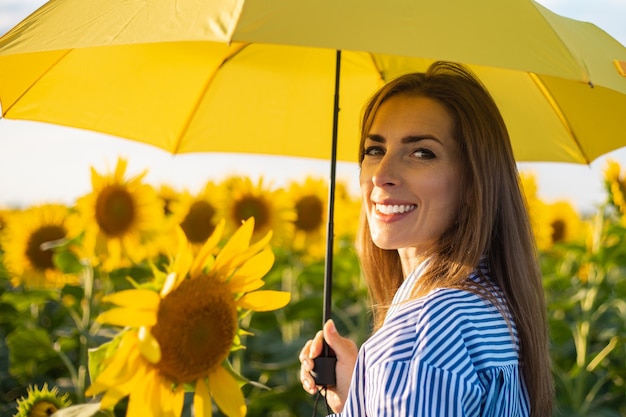 Mujer joven en vestido y paraguas amarillo en un campo de girasoles.