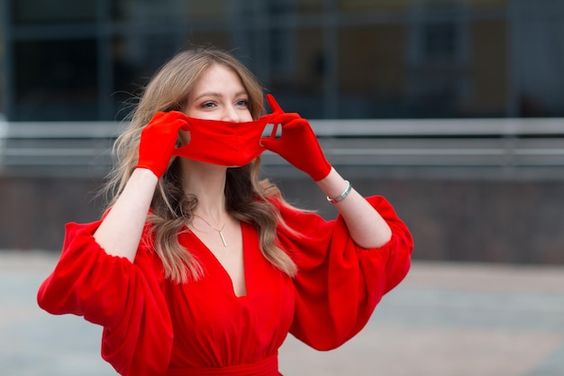 Mujer joven con vestido rojo y guantes se pone una mascarilla protectora médica