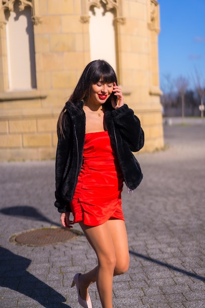 Mujer joven con vestido rojo en un hermoso castillo caminando y hablando por teléfono sonriendo