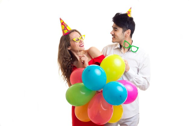 Mujer joven en vestido rojo y joven agradable con sombreros de celebración sosteniendo muchos globos de colores