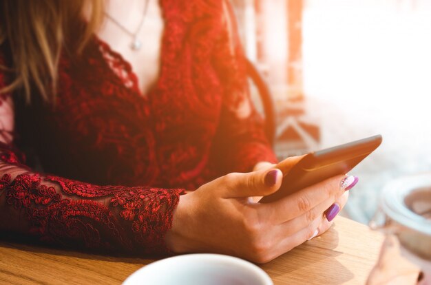 Mujer joven en vestido rojo con Smartphone en cafetería