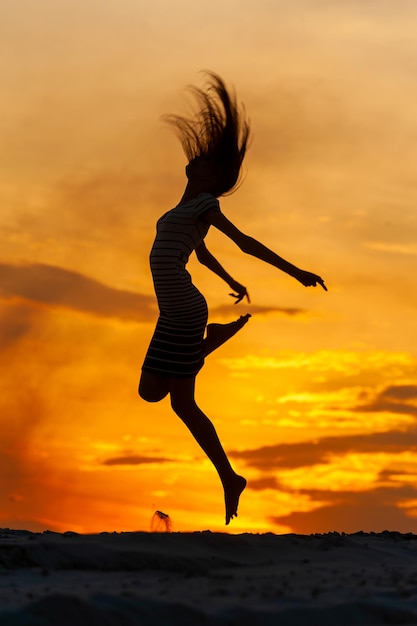 Mujer joven en vestido saltando al atardecer.