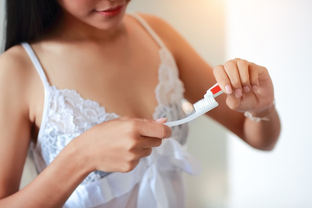 Mujer joven en vestido sexy con cepillo de dientes y colocar pasta de dientes