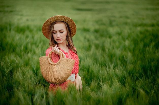 Mujer joven en vestido y sombrero en campo verde de cebada en campo.