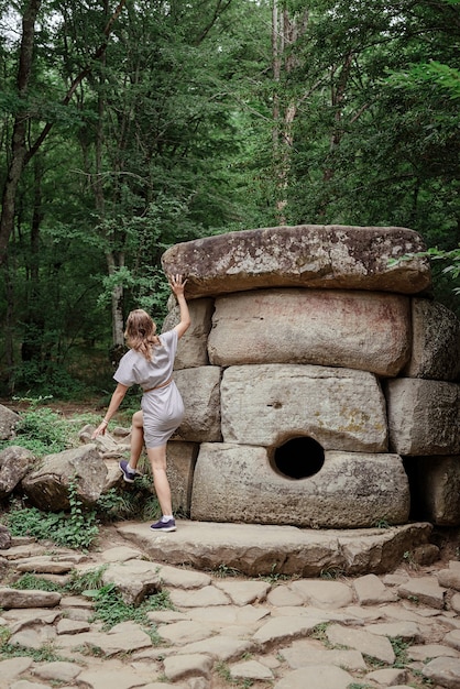 Mujer joven en vestido de verano caminando cerca de la gran piedra del dolmen en el bosque