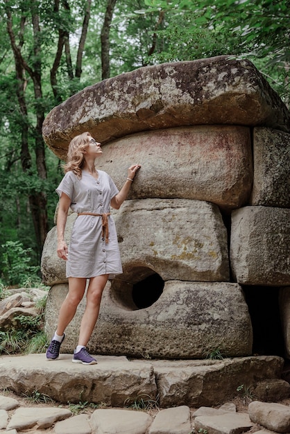 Mujer joven en vestido de verano caminando cerca de la gran piedra del dolmen en el bosque