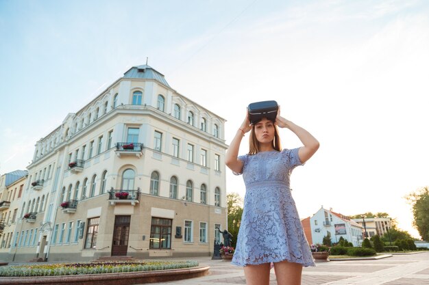 Mujer joven en vestido de verano con dispositivo VR al aire libre.