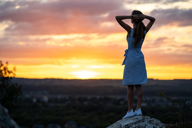 Una mujer joven en vestido de verano de pie al aire libre disfrutando de la vista del atardecer amarillo brillante.