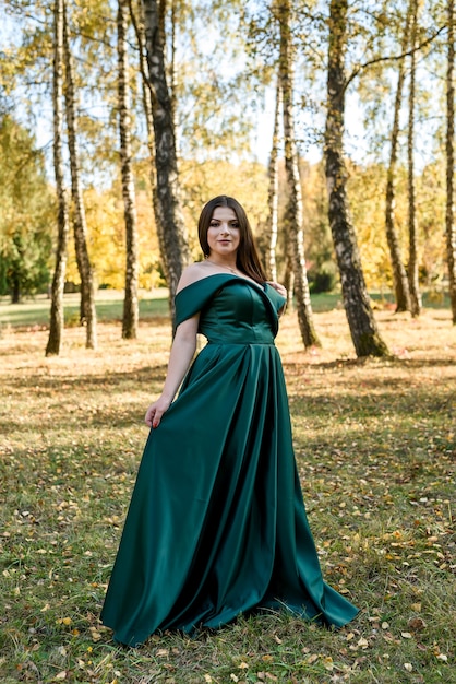 Mujer joven con vestido verde de moda caminando en el parque de otoño.